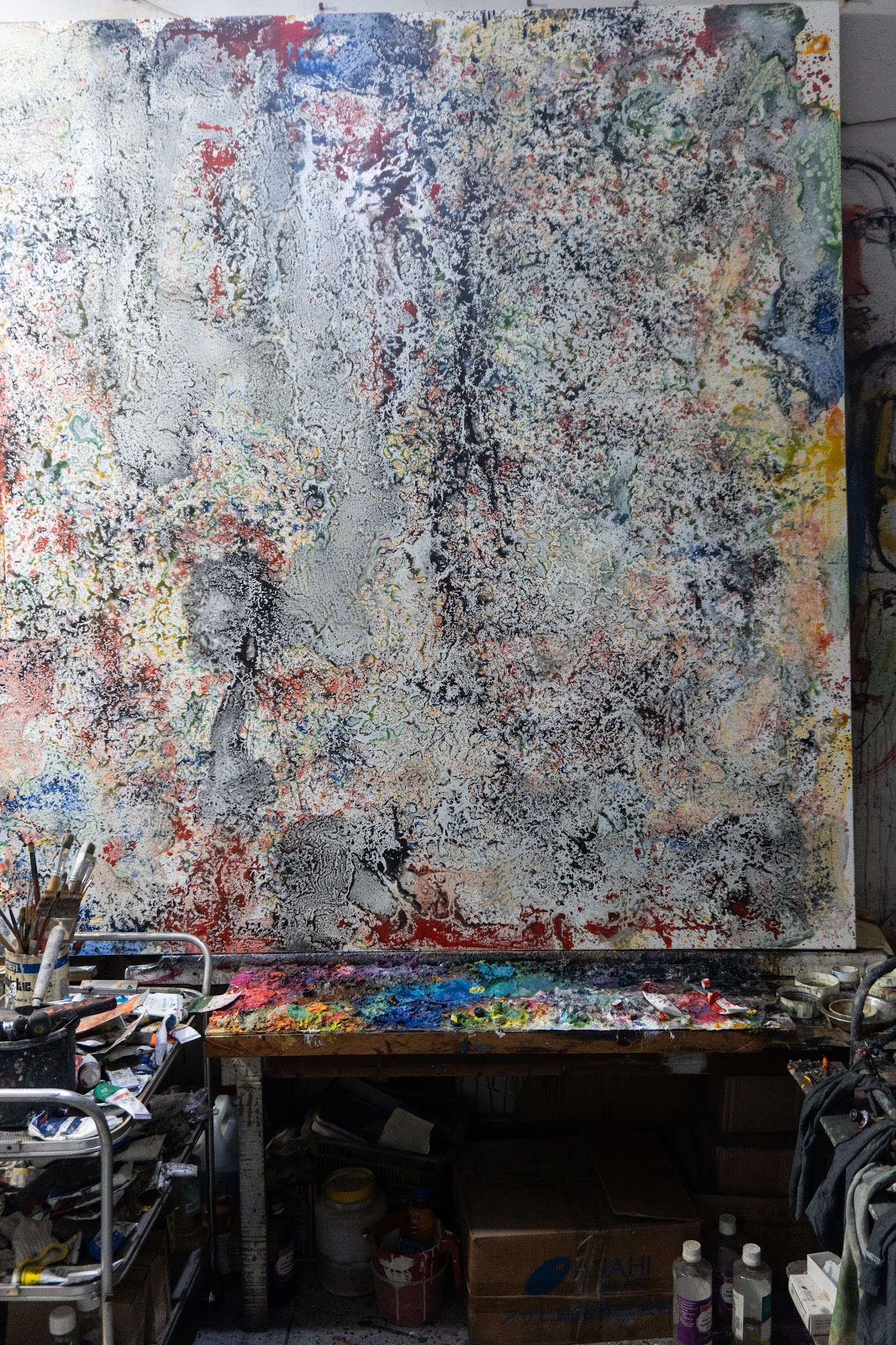 A large white and black textured canvas on an easel, with a paint-caked palette below