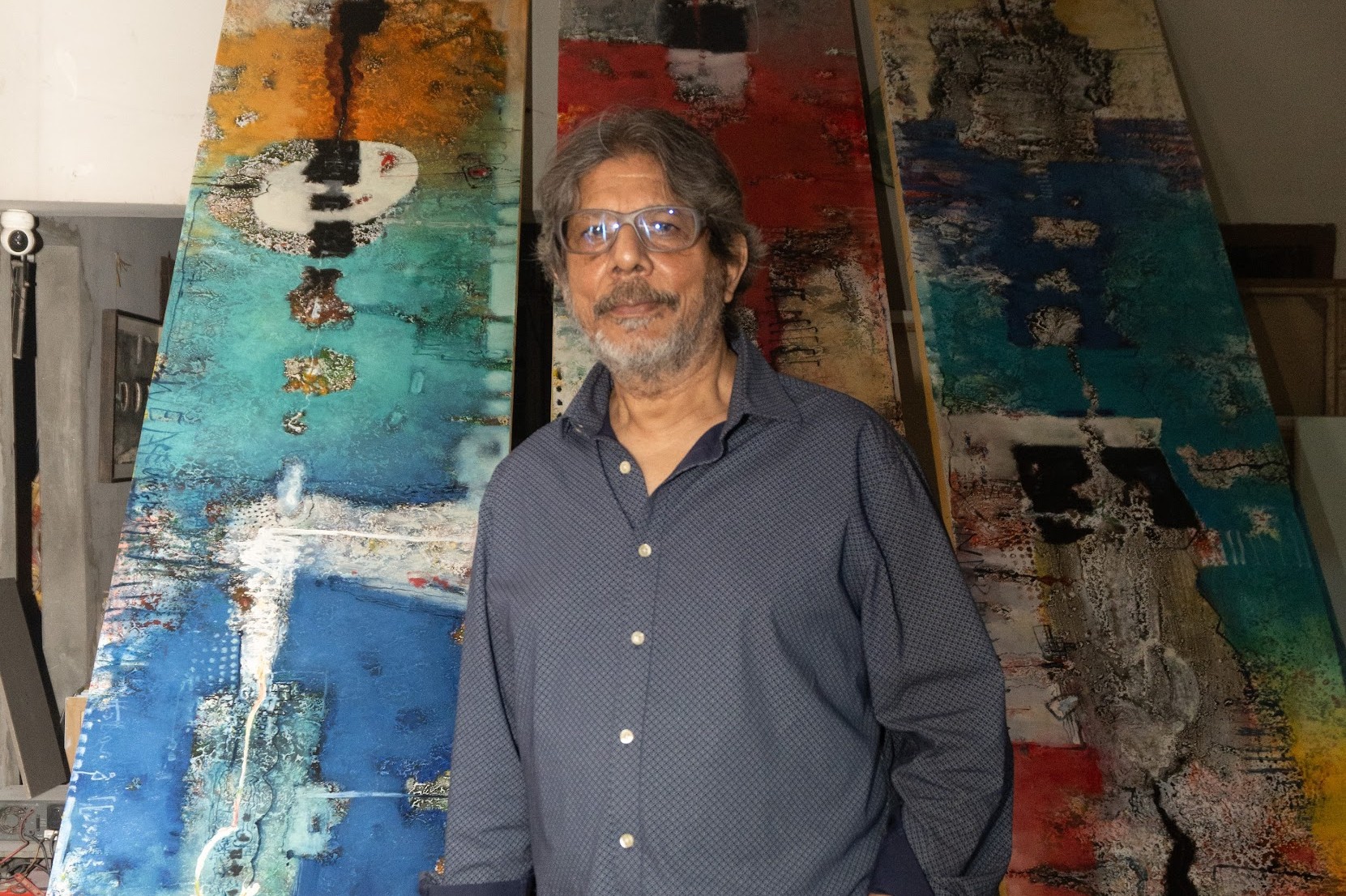 Mohammad Eunus standing among three tall abstract panels in his studio